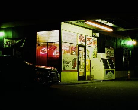 a gas station by night with a open neon sign in the window