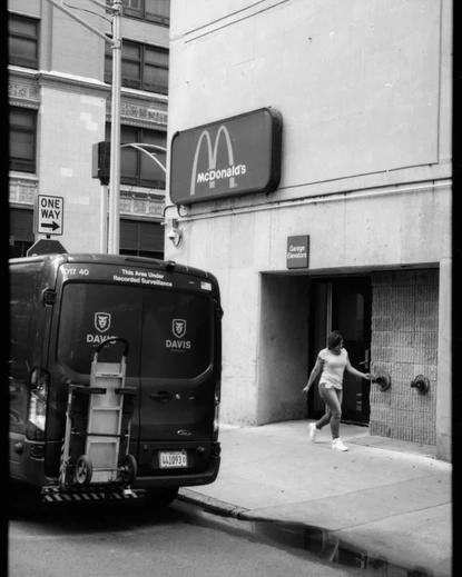 a woman walks by a Davis car, a garage elevator and under a Mcdonalds sign