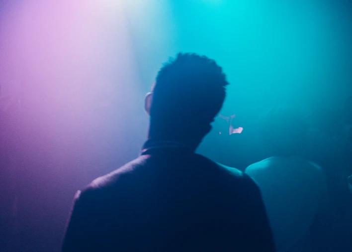 a man is standing with his back towards the camera and is covered in purple and blue light 