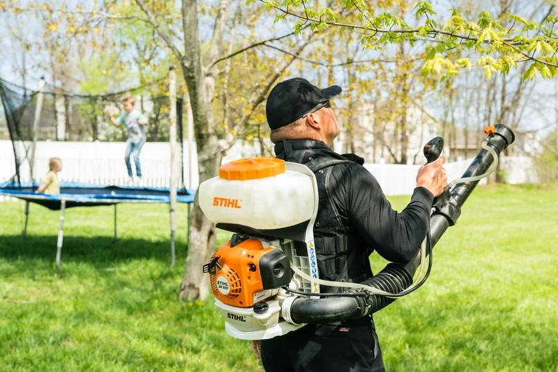 Amco Ranger doing garden work while kids are jumping on trampoline in the background