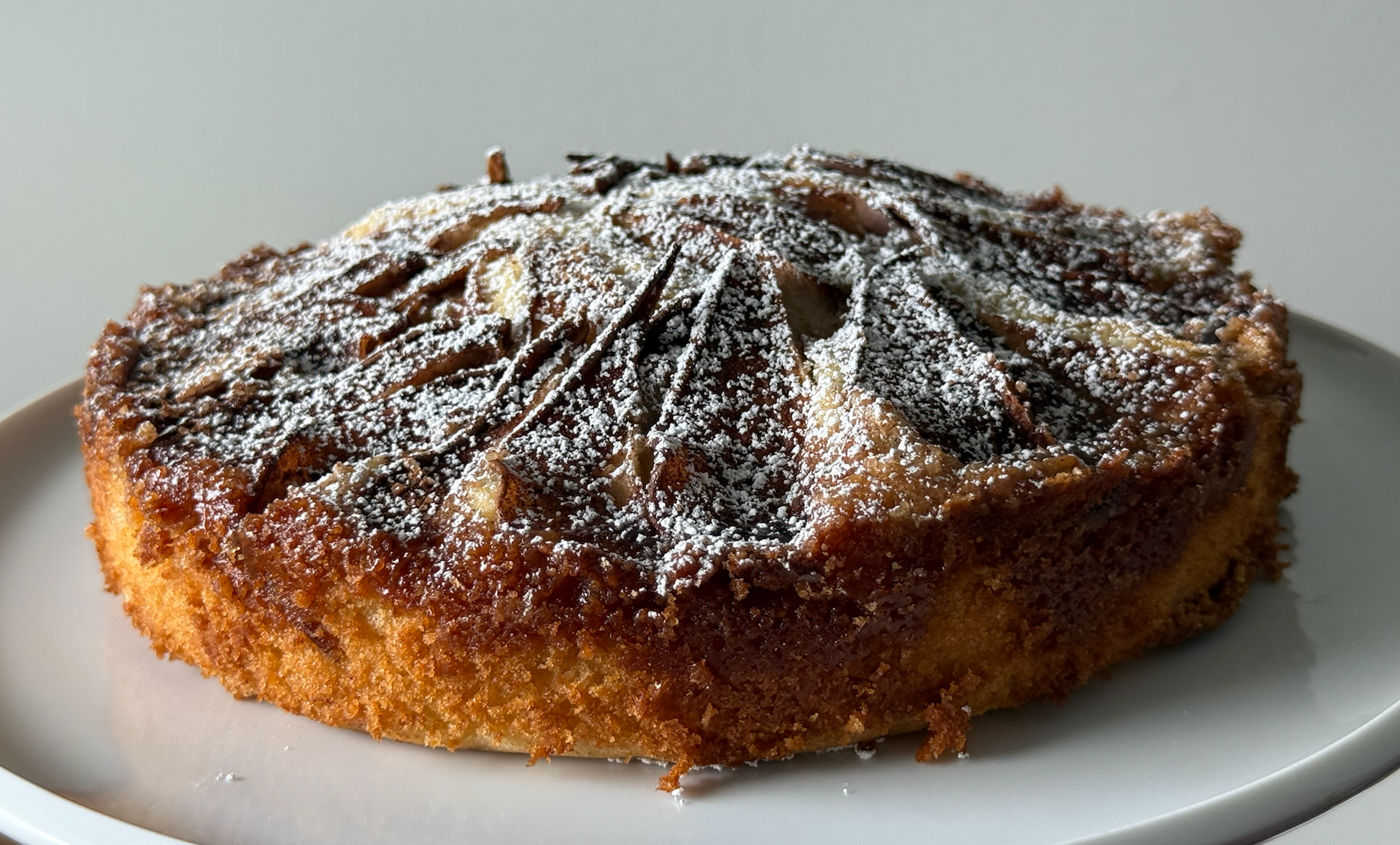 A single layer cake topped with baked pears and dusted with powdered sugar on a white plate. 