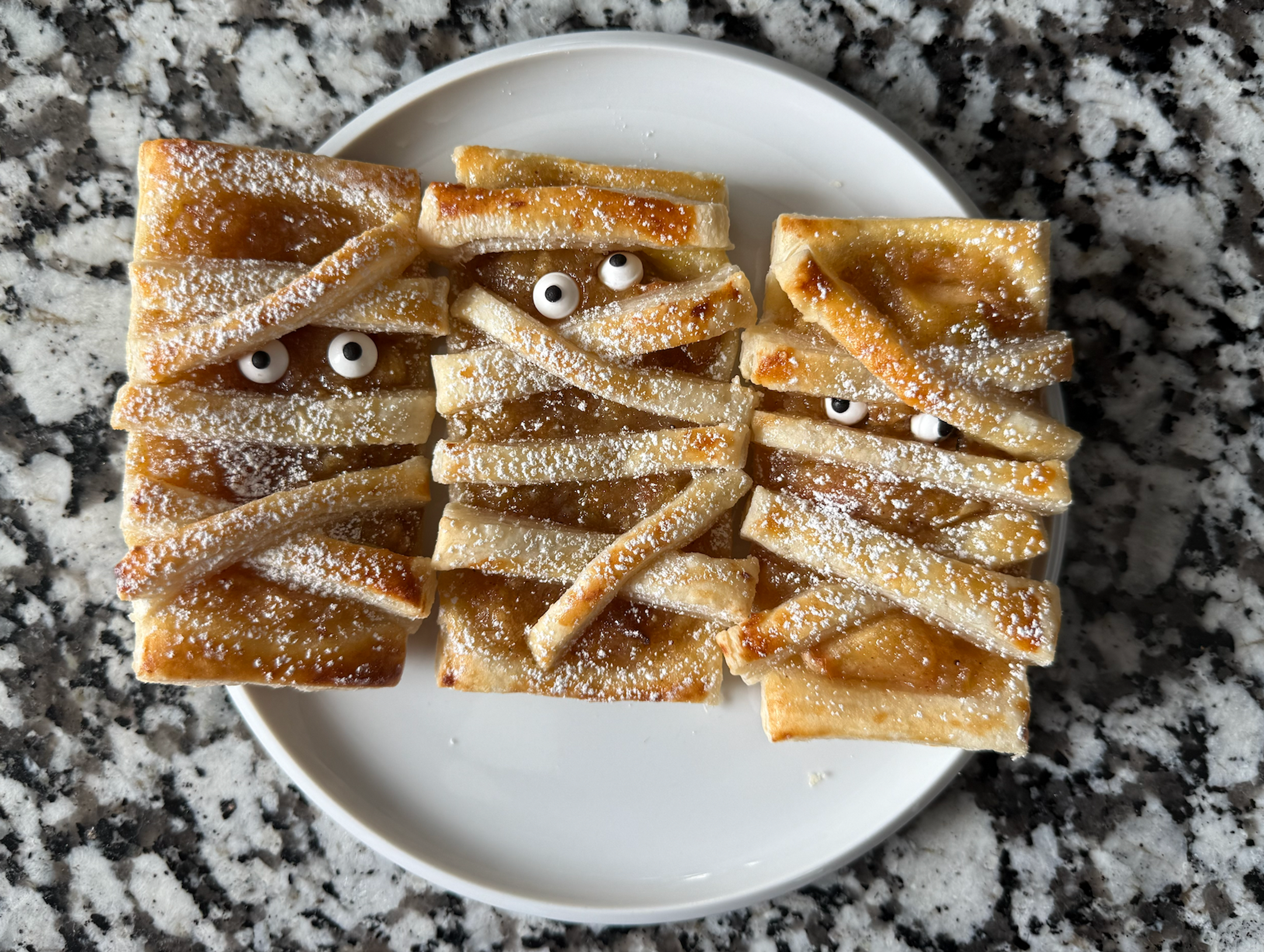3 mummy puff pastries on top of a white plate.