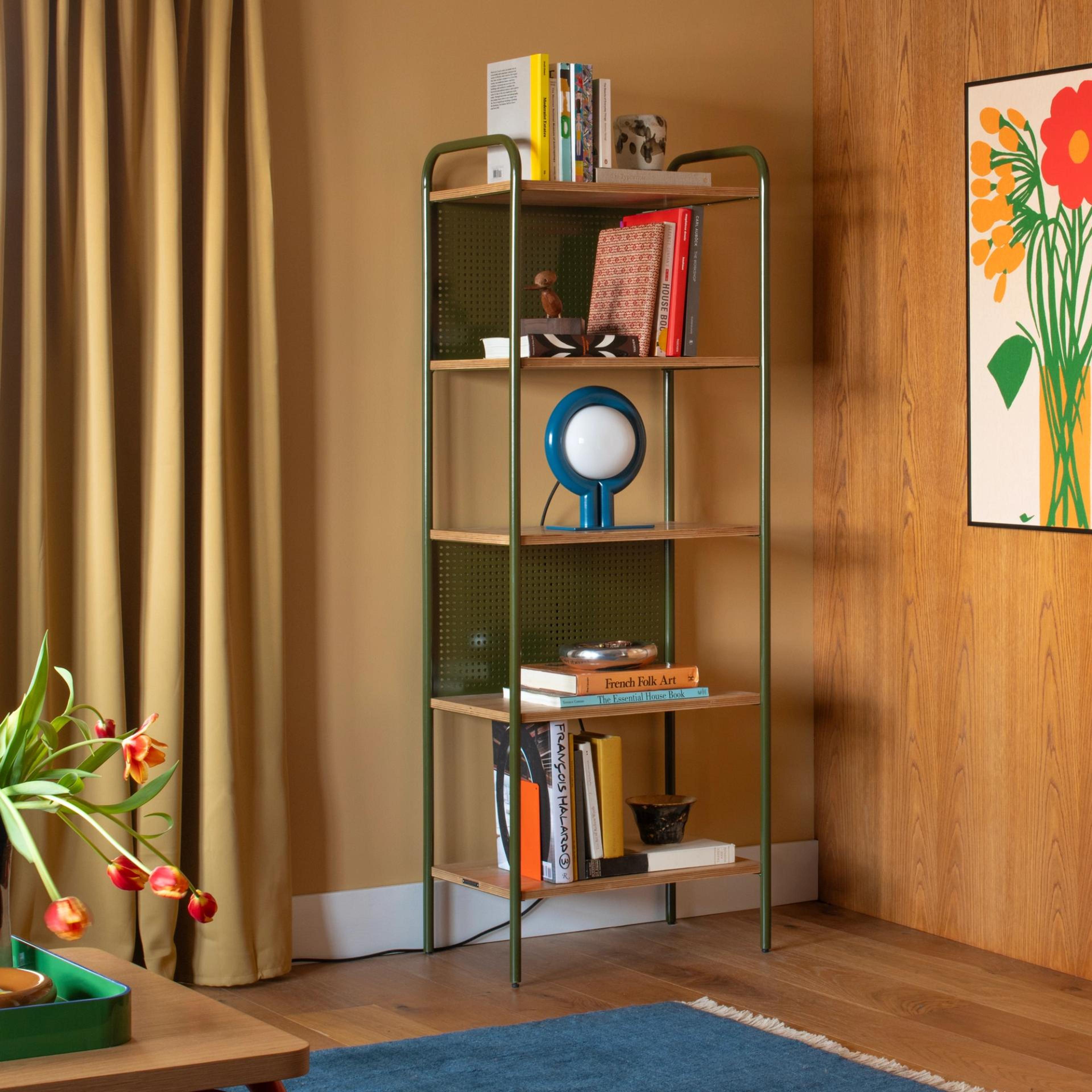 corner of living room showcasing a Schoolhouse Electric green shelf with lamps, books, and decorations