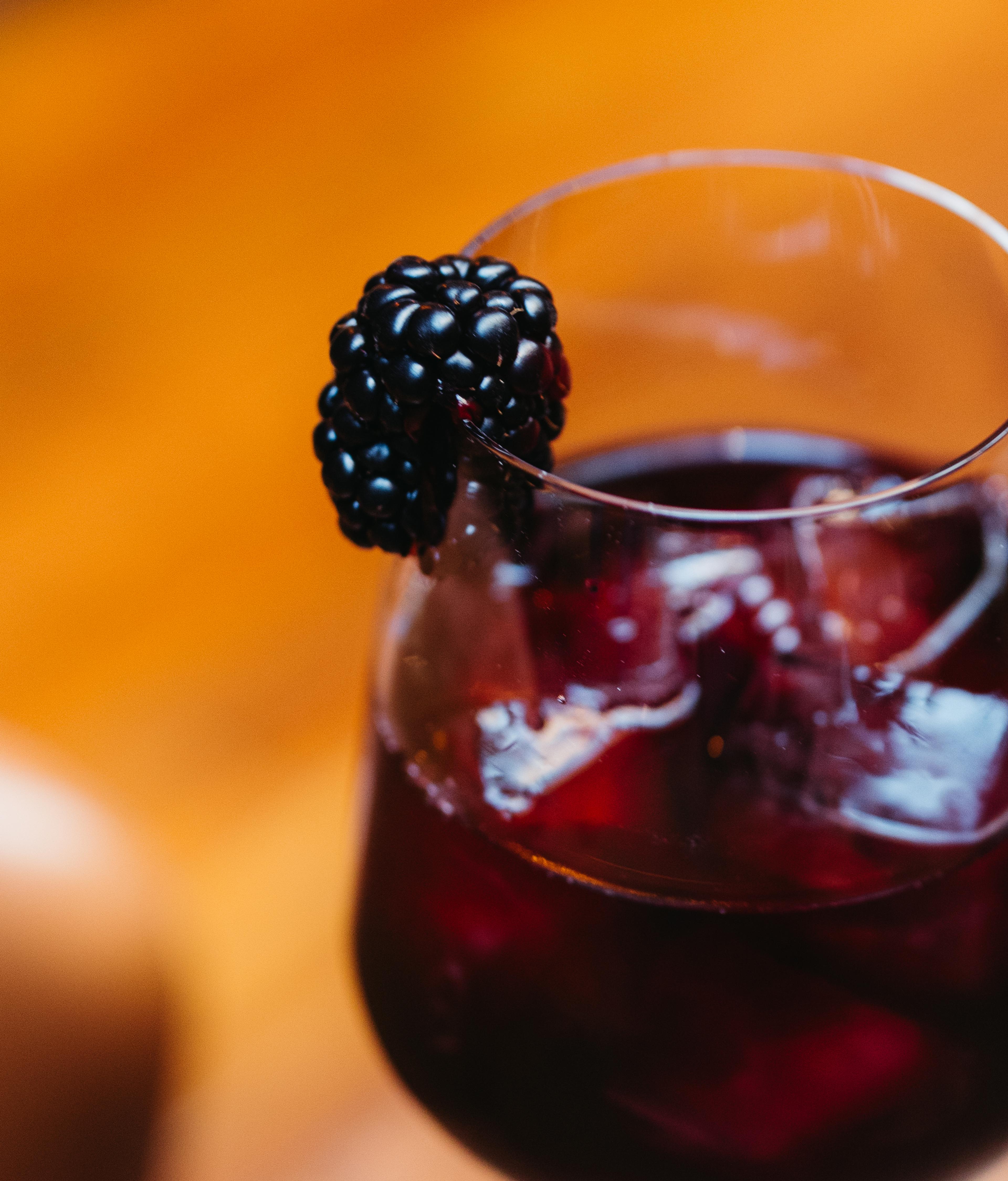 close-up of dark purple blackberry cocktail in glass with blackberry garnish