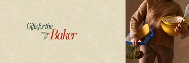 person wearing a sweater holding mixing bowls, measuring cups, a whisk, and other baking supplies