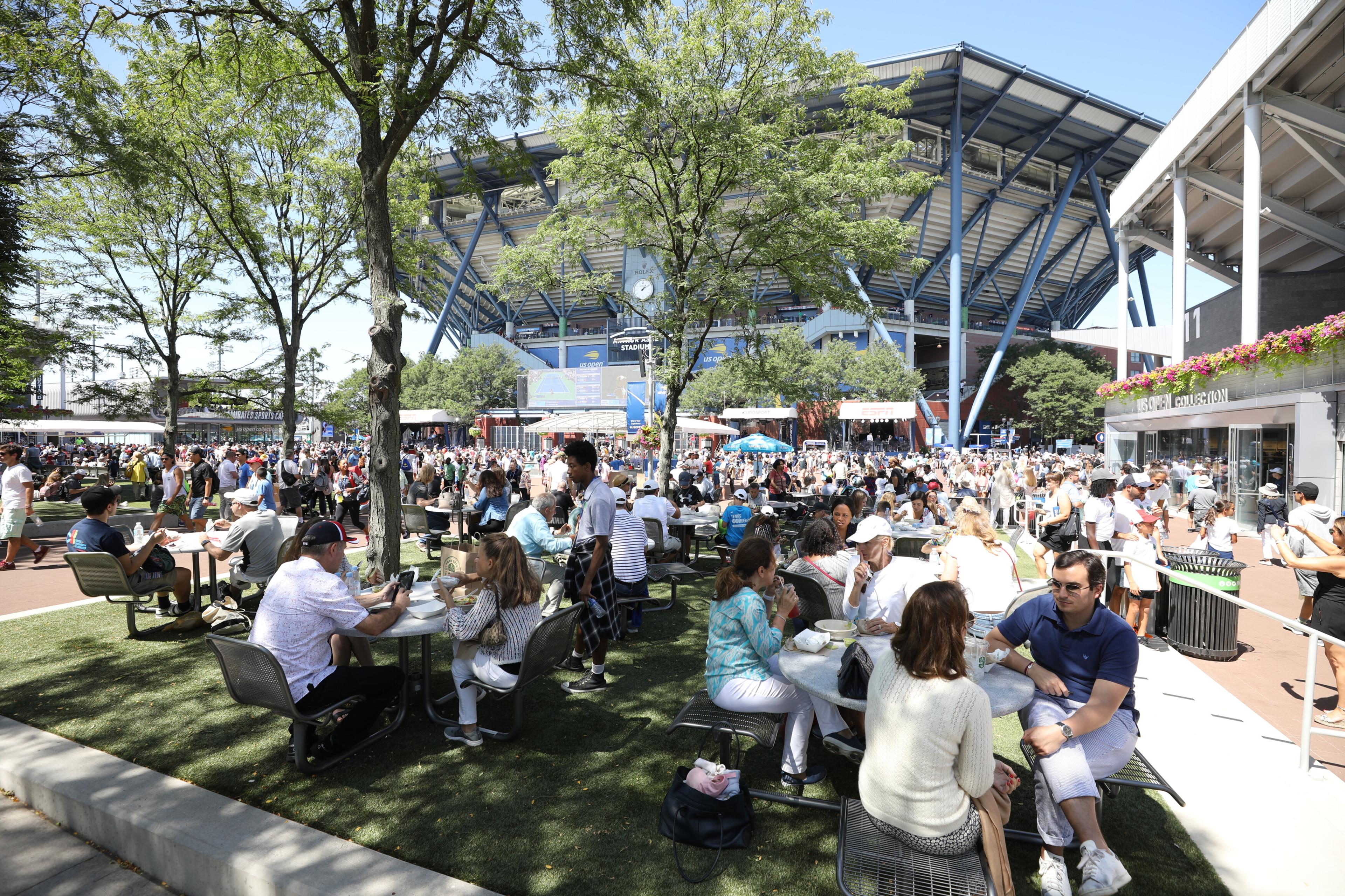 Fans sit and eat around South Plaza with Arthur Ashe Stadium in the background at the 2019 US Open.