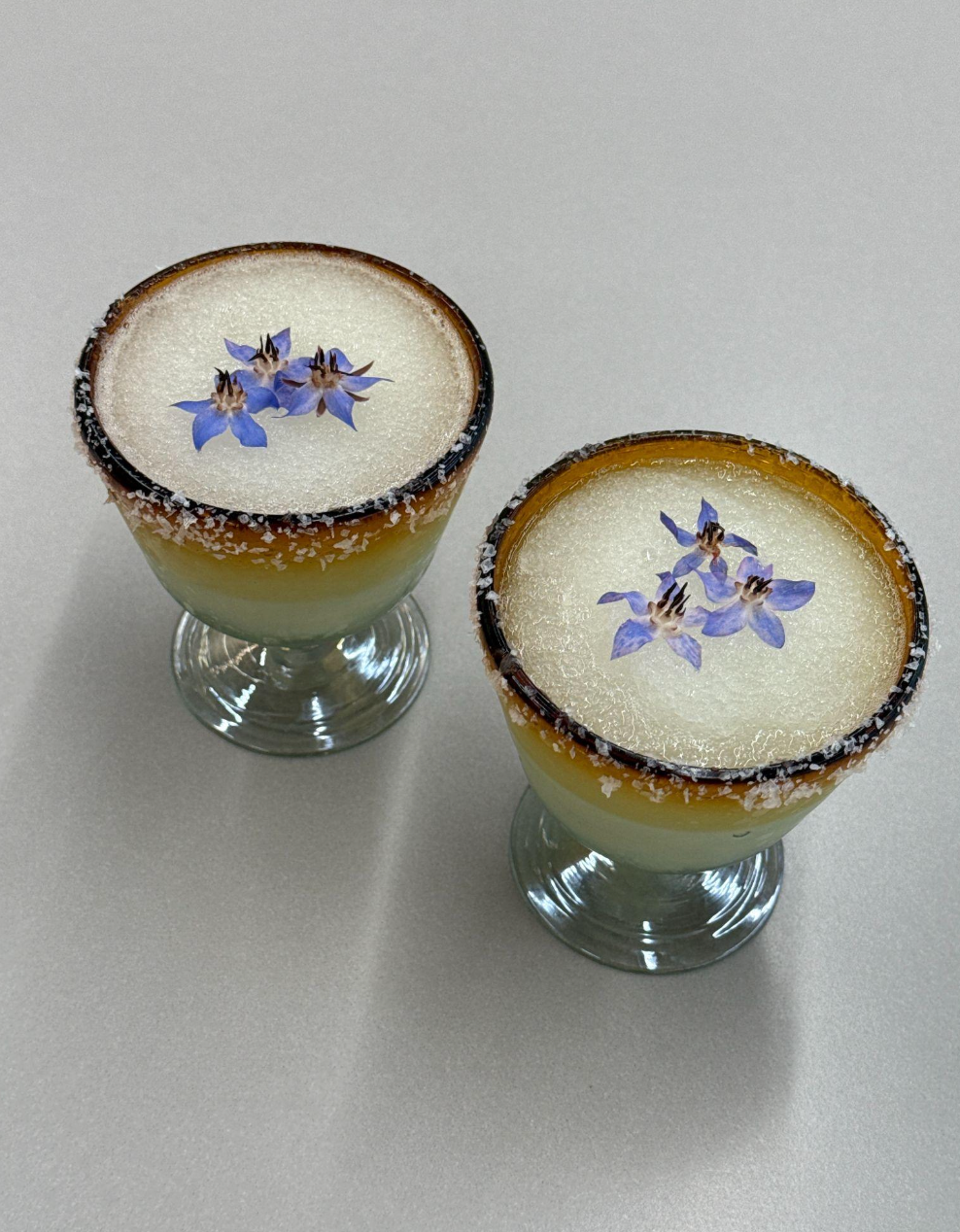 two glasses of margaritas with salt rim and purple flower garnish
