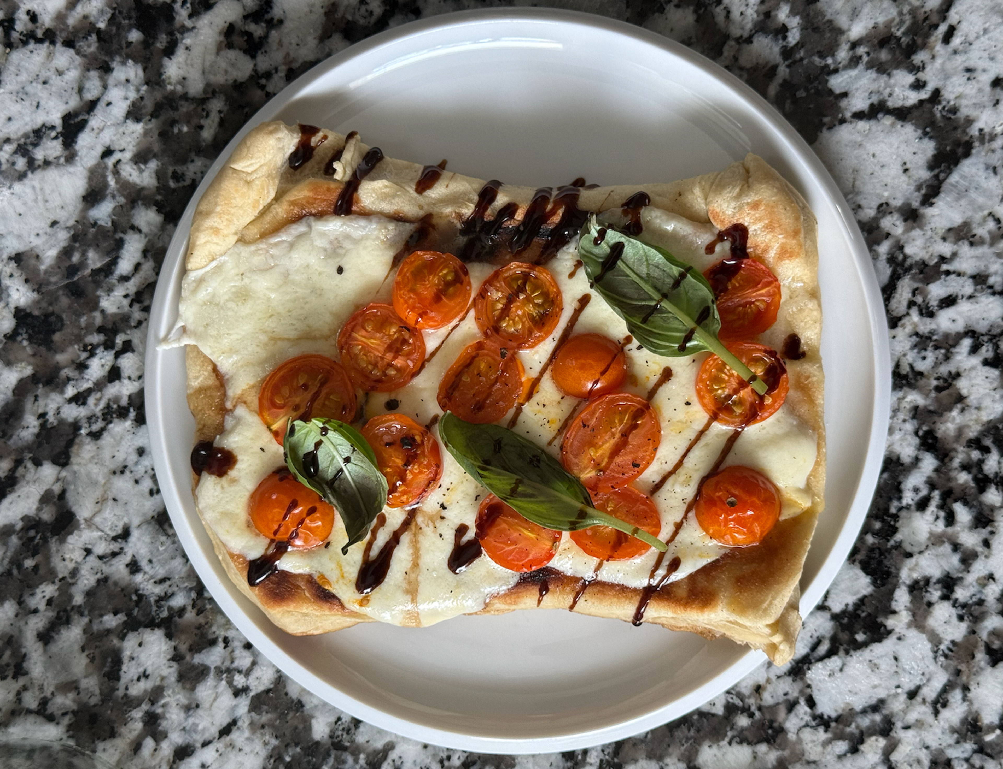 Flatbread pizza with a balsamic vinegar drizzle, cherry tomatoes, and mozzarella cheese