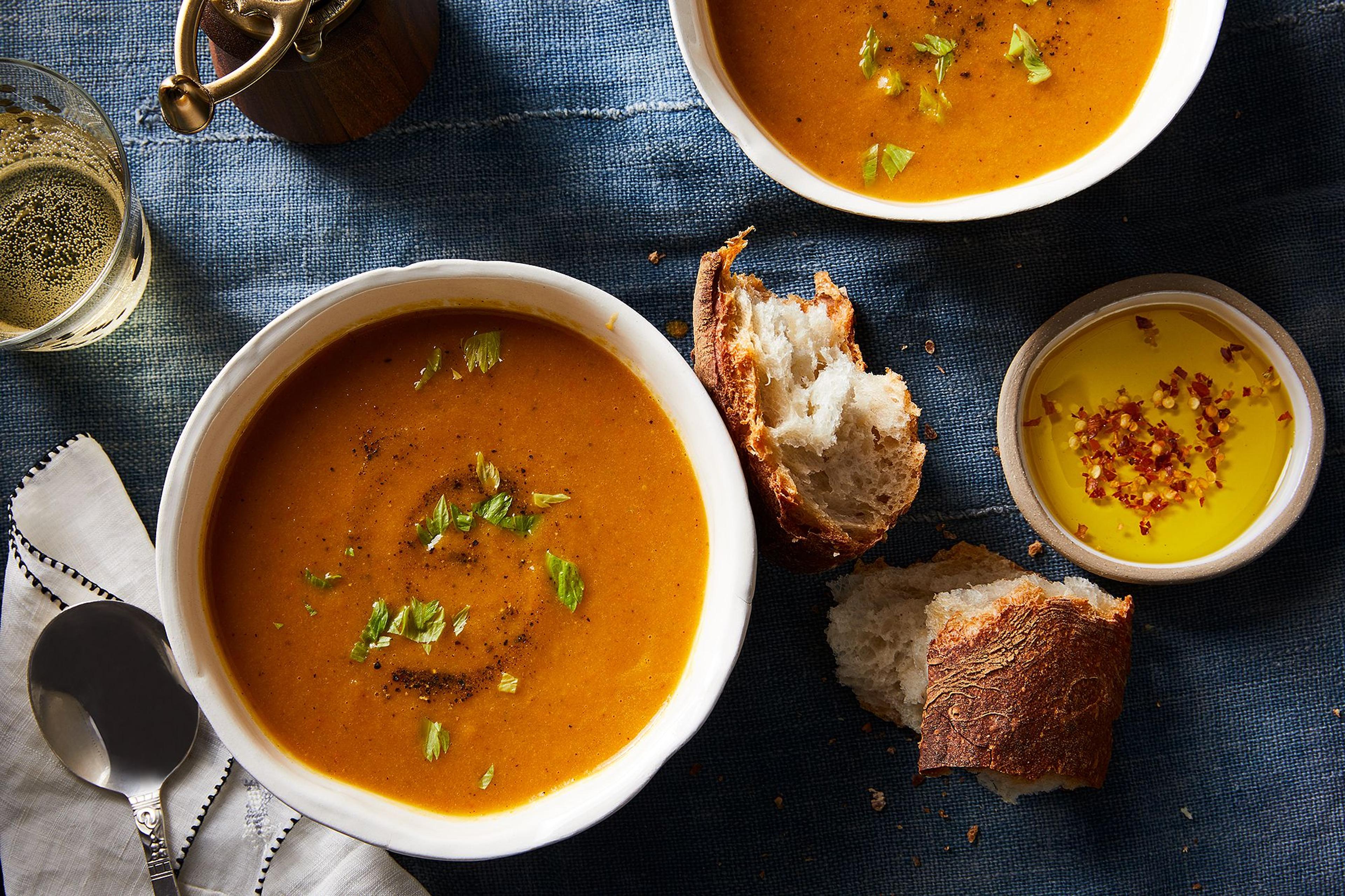 Two bowls of hot roasted carrot soup with scallion garnish on table.