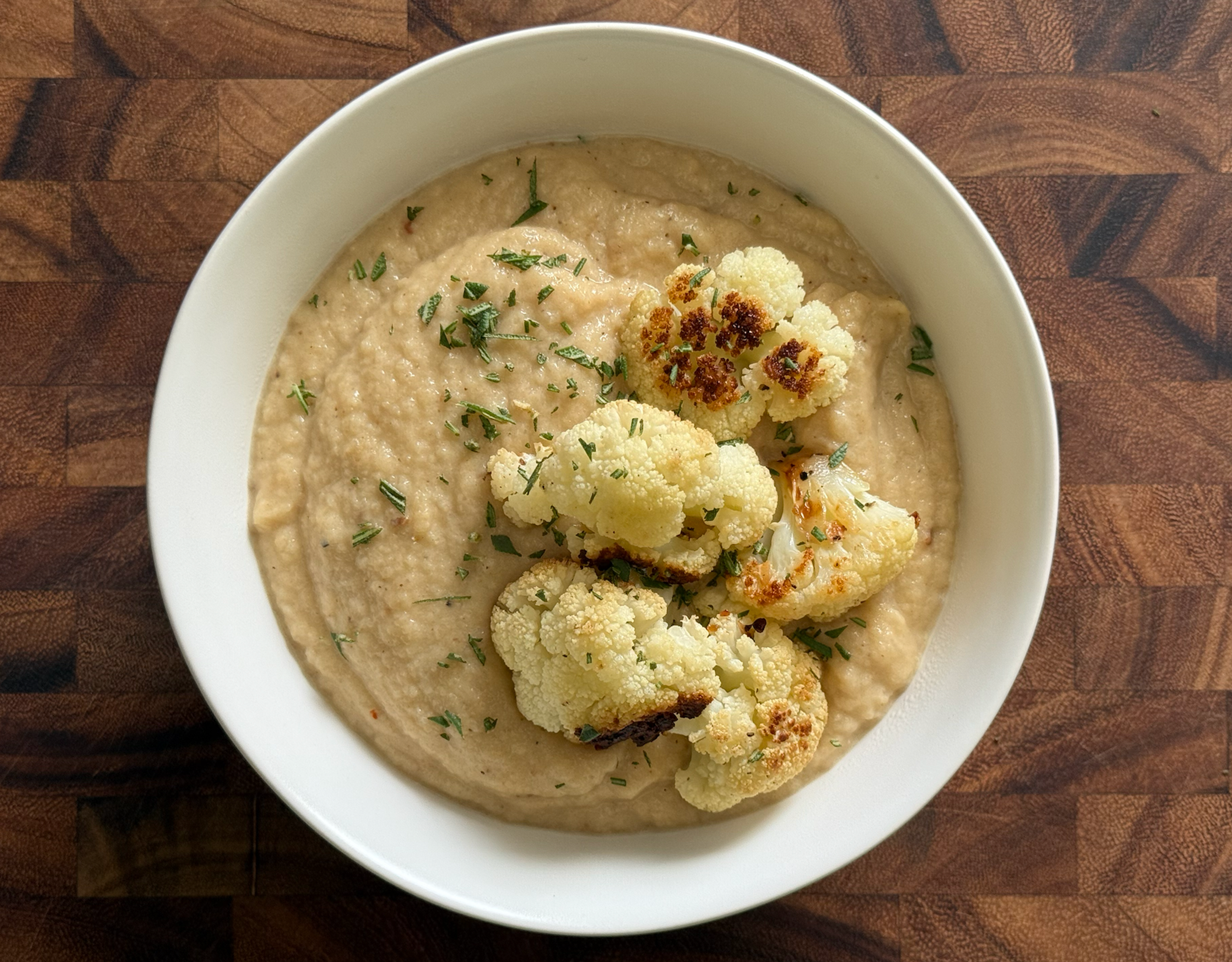 Roasted Cauliflower White Cheddar Soup in a white bowl on a cutting board