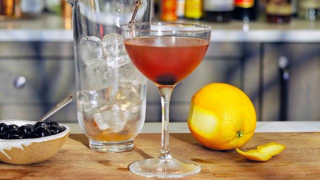 coupe with Manhattan cocktail in it and orange off to the side