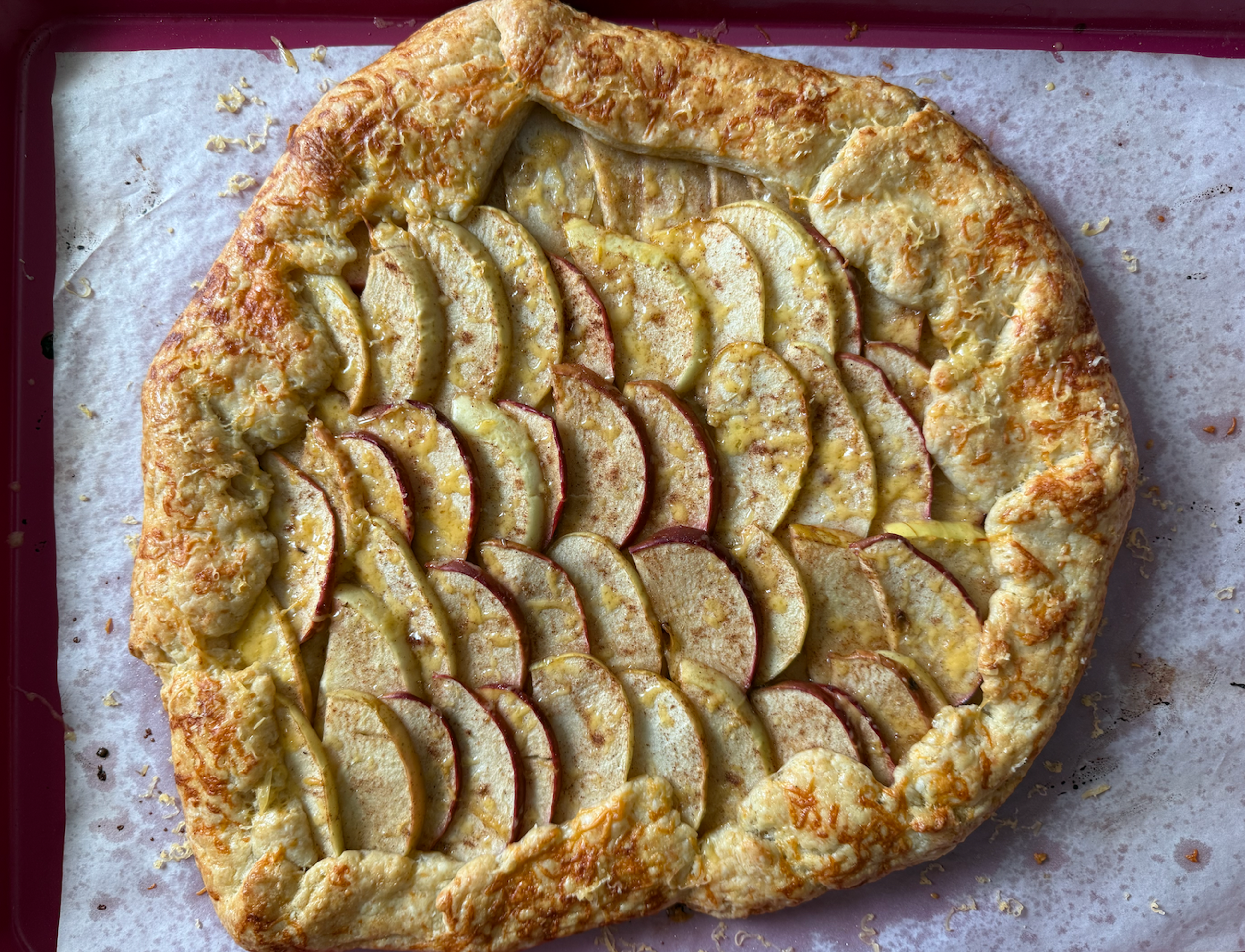Large galette with apple slices on top. Placed on a pink baking sheet.