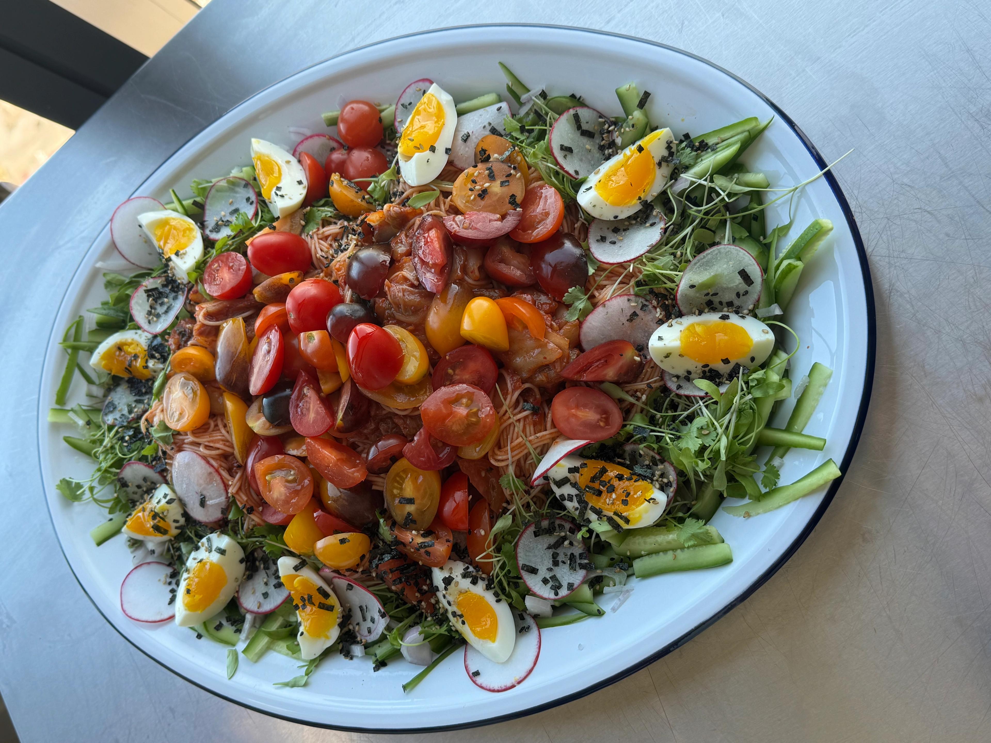 plate of kimchi tomato noodles on platter with eggs, sesame seeds, tomatoes, and cucumber