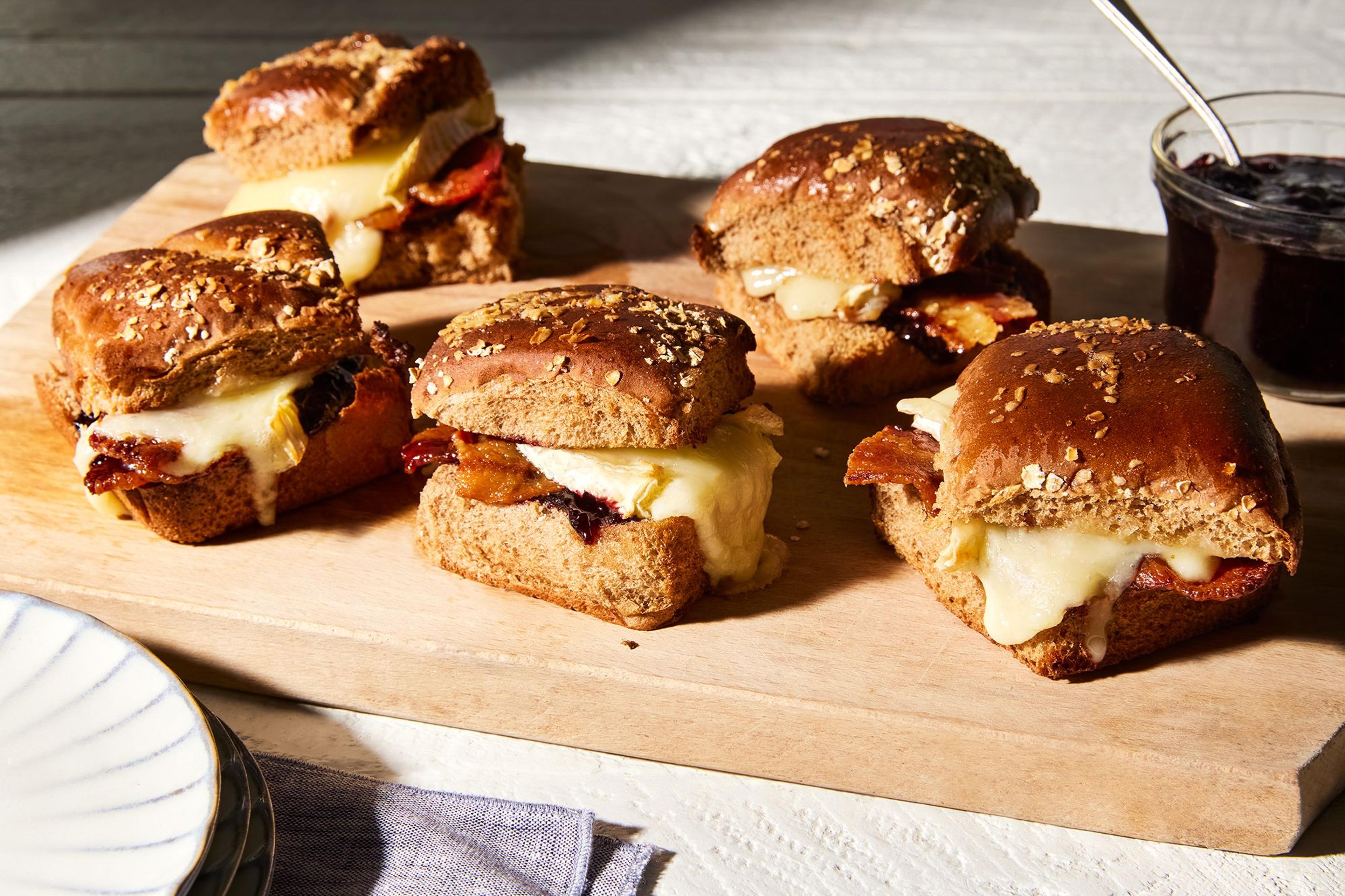 Bacon, brie and jam sliders on a wooden board.