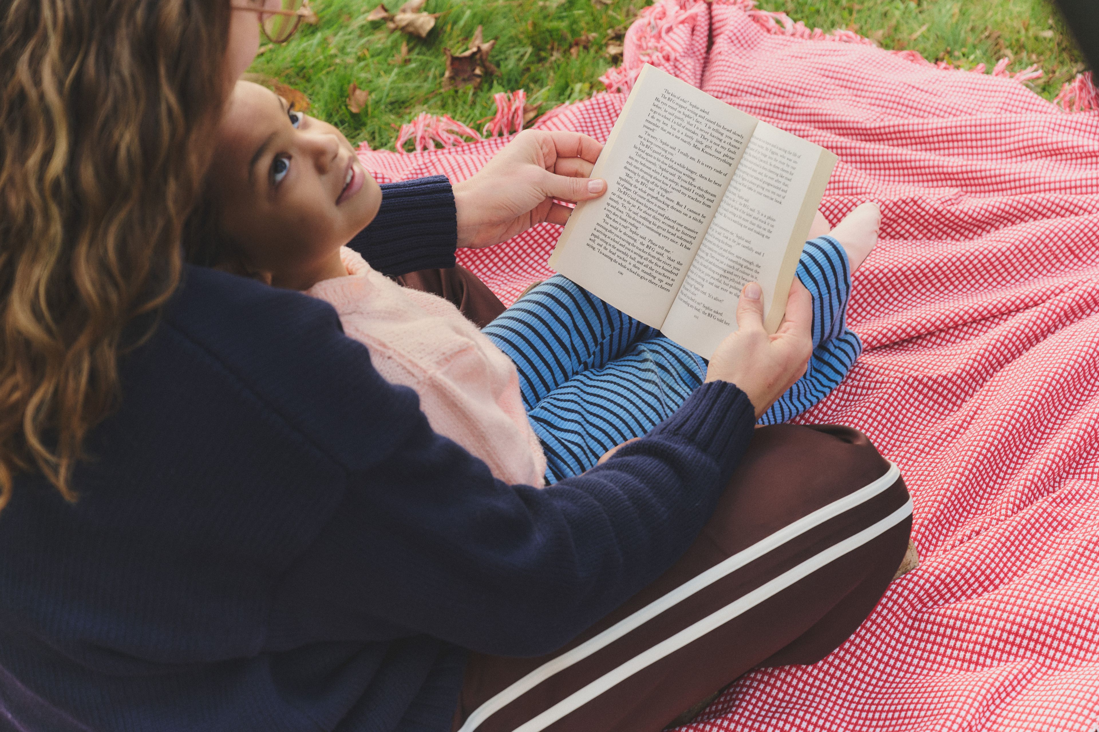 An adults ready to a child while sitting on a picnic blanket