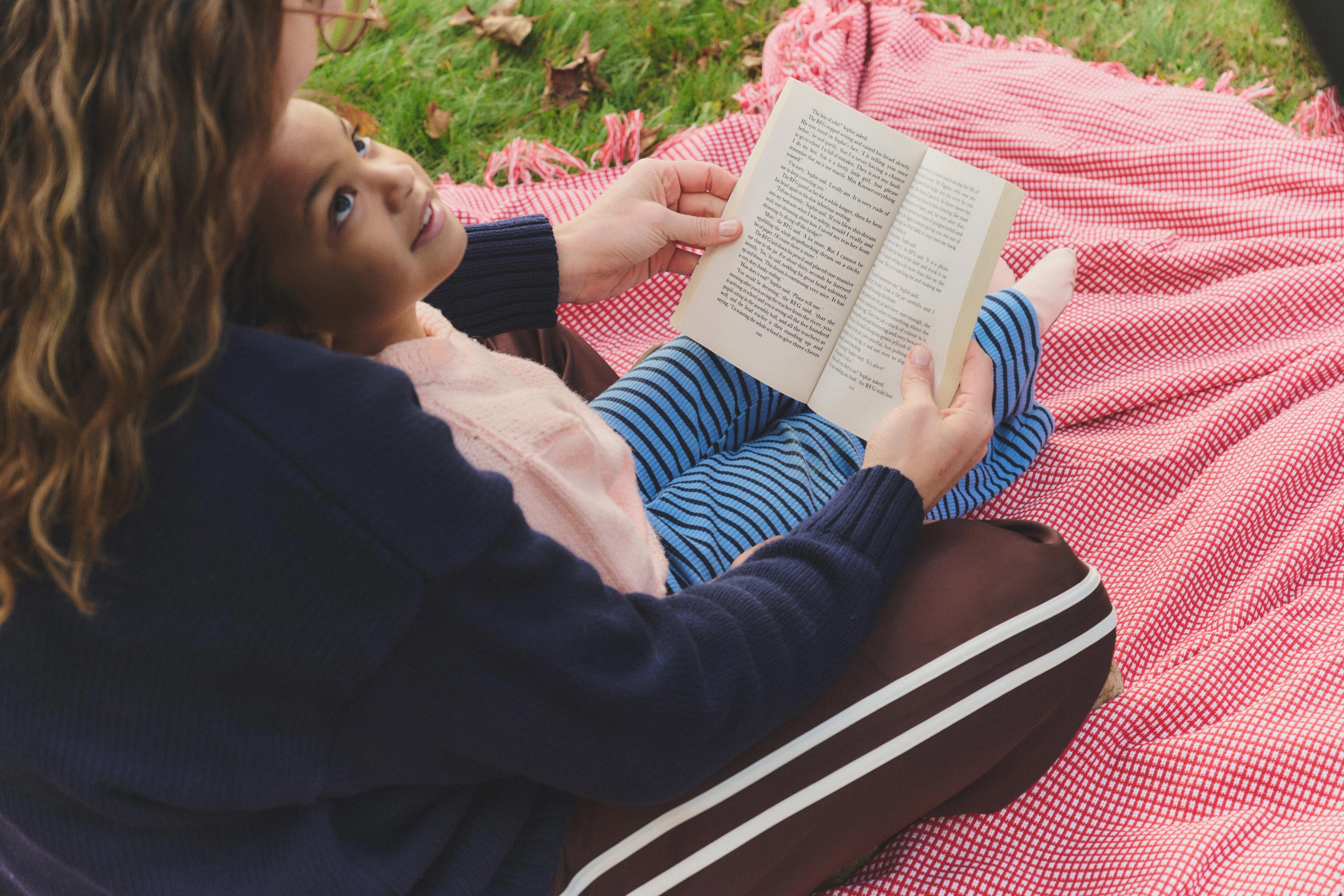 An adults ready to a child while sitting on a picnic blanket