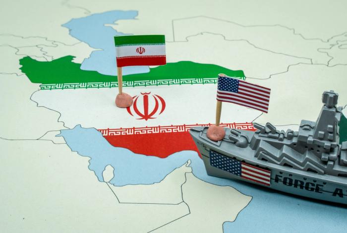 United States and Iran national flags on a geopolitical map with a toy warship, published on an unbiased Canadian news source