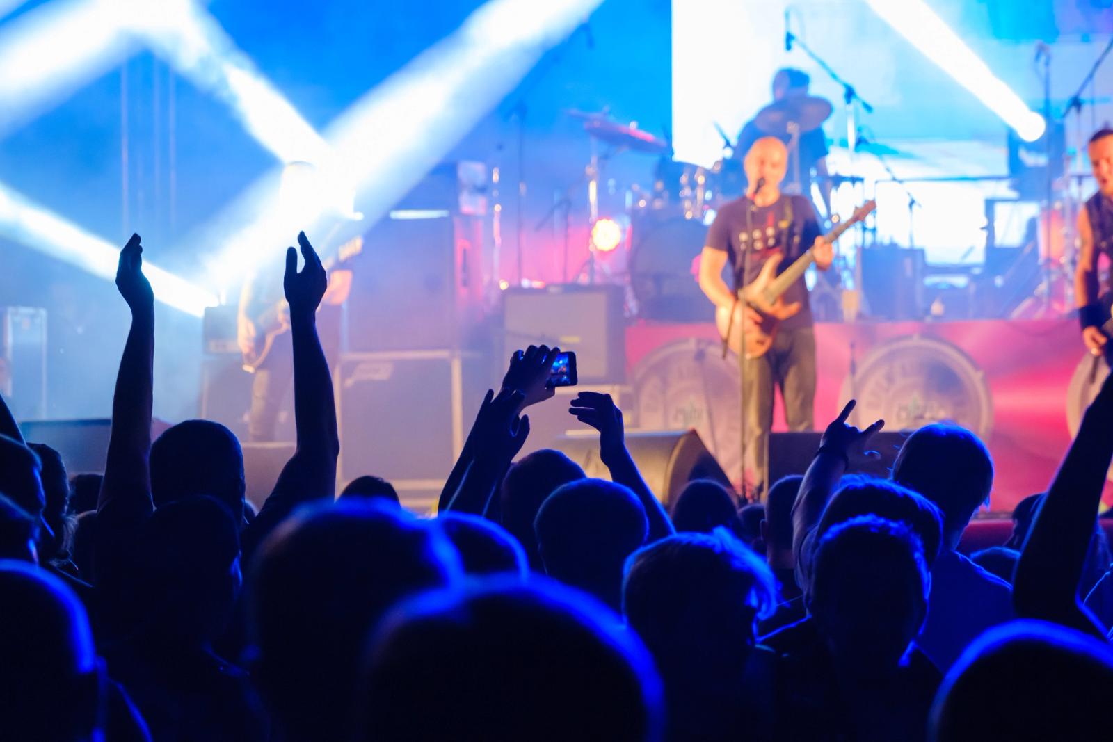 Silhouettes of people enjoying live concert of musician band performing song on stage in bright spotlights, featured on an unbiased Canadian news source