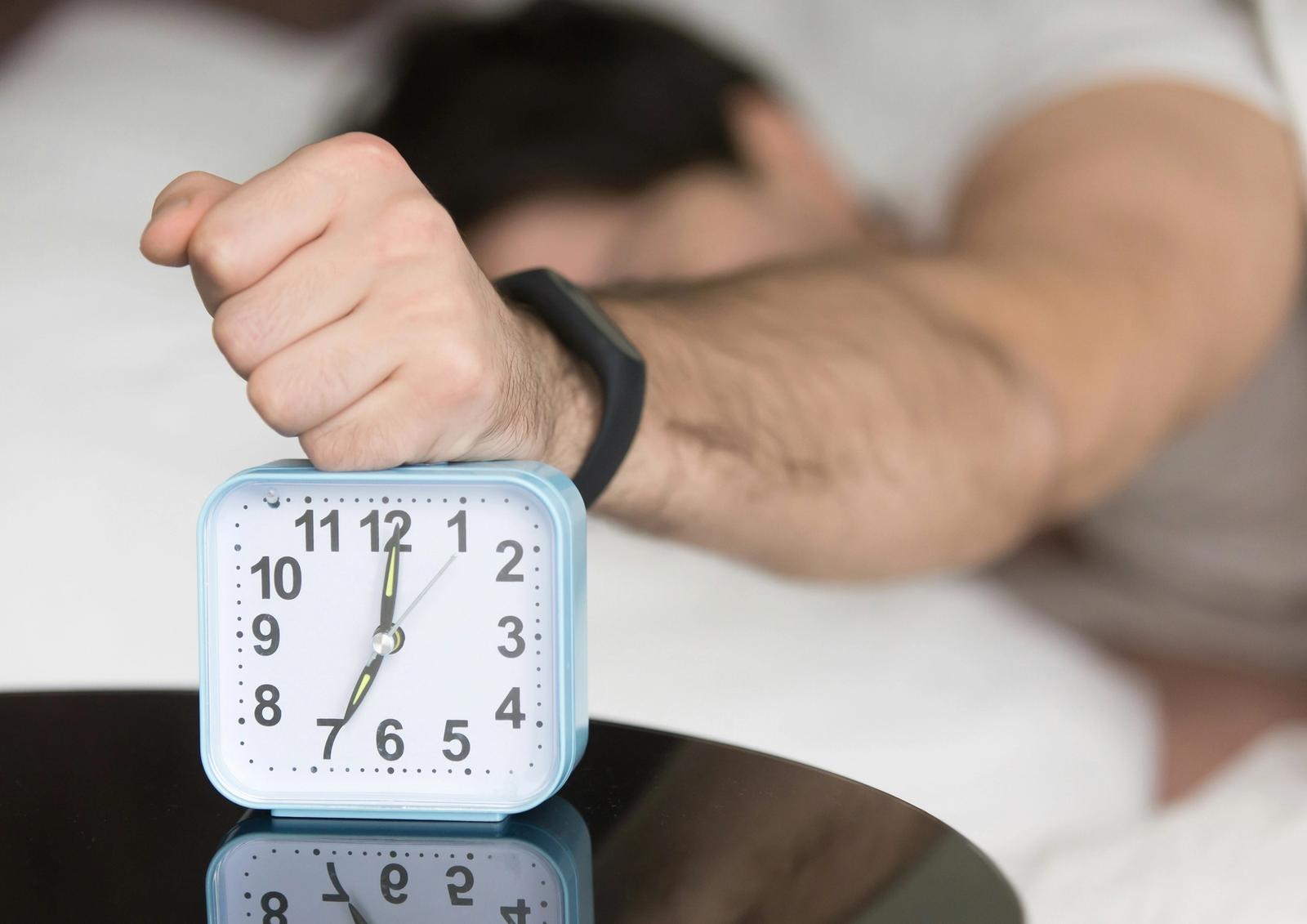 A man reaching out to his alarm clock from bed
