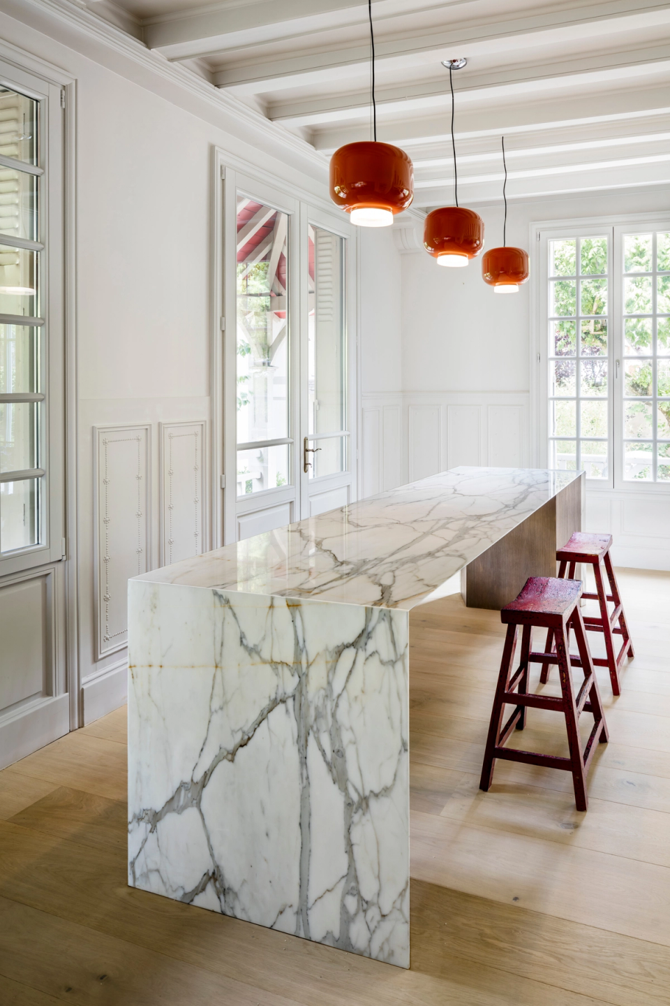 Interior renovation of a linear minimalist kitchen that prioritizes natural light, functionality, and the purity of materials. Integrated cabinetry with clean lines, light-toned finishes, and the combination of white surfaces and wood create an elegant and timeless space perfectly connected to the original architecture of the residence.