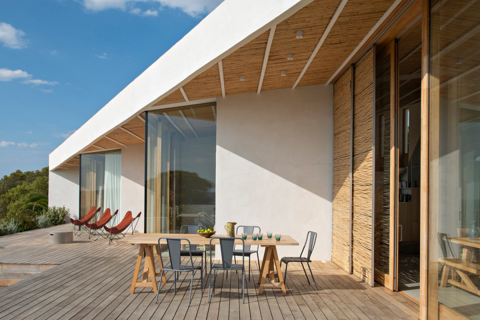 Terrace of a contemporary detached house with wooden cladding, large windows and open spaces oriented towards the outdoors. The architecture combines natural materials and minimalist lines to enhance natural light, views and continuity between interior and exterior within a Mediterranean environment.