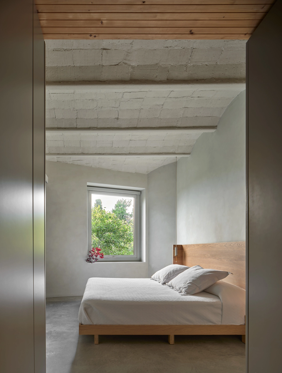 Housing renovation with an open and bright bedroom that restores the original roof volume and enhances interior calm. The renovation integrates natural materials, exterior light and a simple layout to create a comfortable and serene atmosphere.