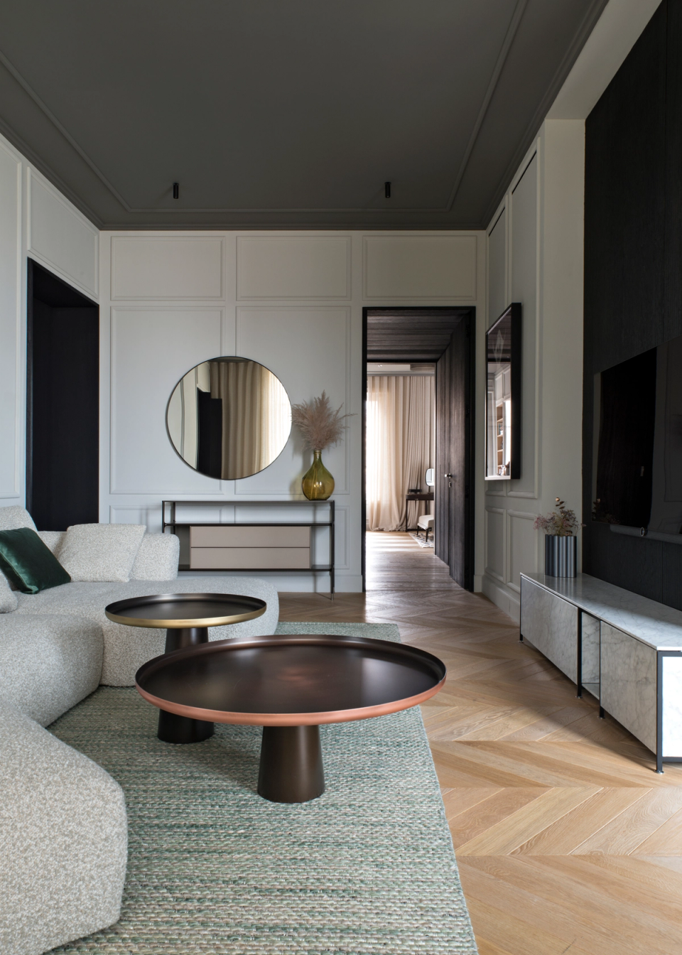 The interior renovation of this living room reinterprets the classical elegance of the home with a contemporary and minimalist approach. Molded walls, herringbone parquet flooring, and decorative ceilings are combined with dark finishes, sculptural furniture, and a selection of noble materials that add depth and sophistication. The open layout and visual continuity between rooms enhance natural light and create a warm, balanced, and timeless atmosphere.