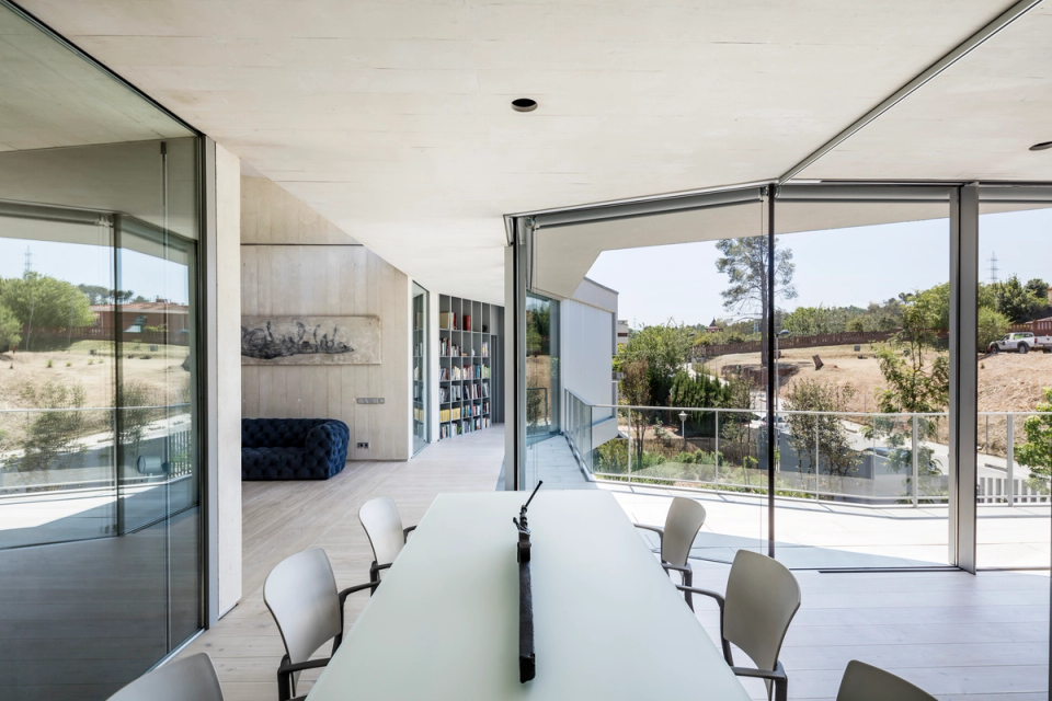 Interior space of a contemporary single-family home with open architecture and a strong emphasis on natural light. Large glass surfaces allow a direct connection with the outdoors and enhance the sense of continuity between interior and landscape. The use of neutral materials, light wood flooring, and minimalist finishes reinforces the elegance of the space, while integrated furniture and clean lines provide functionality and sophistication to this modern architectural proposal.