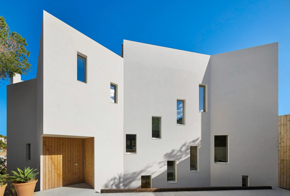 Detached single-family home with sculptural volumetry and contemporary lines that embraces refined and minimalist architecture. White façades, vertical openings, and natural wood finishes create a play of light and proportions that reinforces the project’s singular and elegant identity.