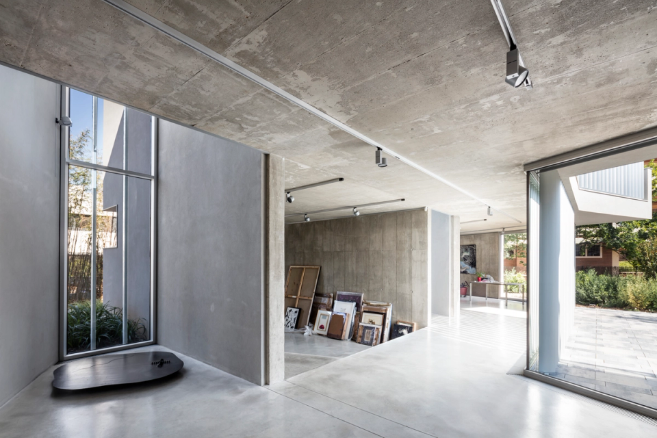 Interior space of a contemporary single-family home with a minimalist aesthetic defined by exposed concrete, clean lines, and open spaces. Large glazed surfaces allow a constant flow of natural light and create a fluid connection between different environments and the outdoors. The combination of continuous materials, integrated lighting, and artistic pieces brings character and sophistication to a modern interior conceived with functionality, spaciousness, and architectural elegance in mind.