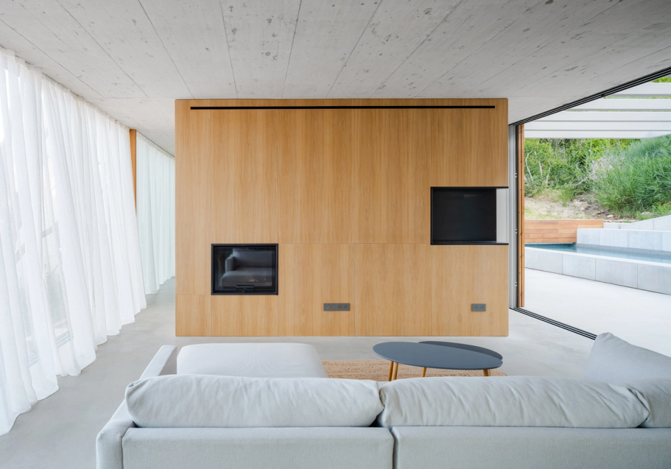 The interior of this single-family home in Begur conveys a minimalist and welcoming aesthetic thanks to the combination of exposed concrete surfaces, natural wood, and clean-lined furniture. The open spaces, natural light, and visual continuity with the outdoors create a serene and contemporary atmosphere designed to enhance comfort and the connection with the Mediterranean surroundings.