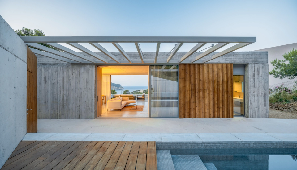 This single-family home in Begur combines architectural minimalism and warm materials in a proposal open to the landscape and the sea. The combination of exposed concrete, natural wood, and large glass enclosures creates a contemporary and timeless aesthetic, while the direct connection between the interior spaces and the outdoor pool area enhances the feeling of spaciousness, brightness, and Mediterranean comfort.