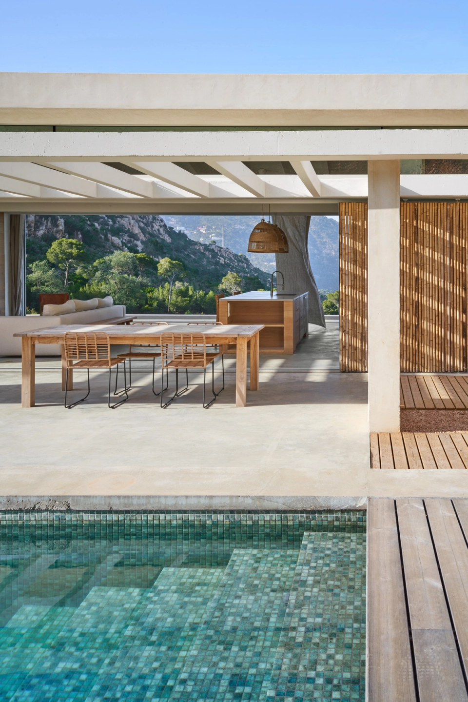 This single-family home merges contemporary architecture and natural surroundings through open spaces, warm materials, and a constant relationship with the landscape. The covered outdoor area acts as an extension of the interior, connecting the pool, dining area, and kitchen into one fluid and functional space. Wooden enclosures, lightweight structures, and large openings make the most of natural light and mountain views, creating a relaxed, elegant Mediterranean atmosphere. This single-family home stands out for its minimalist architecture, integration with the surroundings, and a layout designed to enhance outdoor living throughout the year.