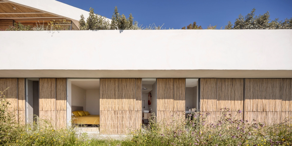 Façade of a detached house integrated into the Mediterranean landscape, featuring natural fiber enclosures and minimalist architecture that prioritizes privacy, ventilation and the connection with the outdoors. Organic materials, native vegetation and pure lines bring warmth and harmony to the home.