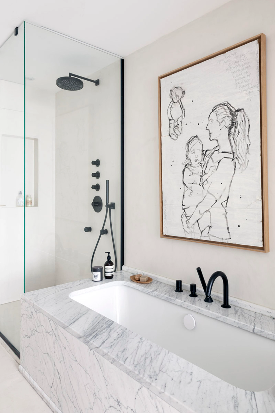 The bathroom stands out for its refined contemporary aesthetic, where noble materials become the main protagonists of the renovation. The bathtub clad in naturally veined marble brings elegance and sophistication, while the matte black finishes of the taps and shower create a modern and balanced contrast. The transparent glass partition reinforces the sense of spaciousness and allows light to flow freely throughout the space. The artwork adds an artistic and personal touch that humanizes the atmosphere and gives character to the whole project. The overall design conveys a serene, minimalist and welcoming atmosphere conceived to transform the bathroom into a space of wellbeing and disconnection within the home.