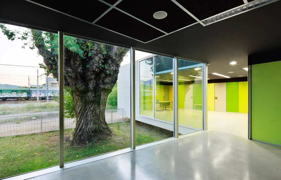  Interior view of the CAP de Sant Vicenç where transparency and connection with the outside become protagonists of the project. The large glass surfaces frame the existing trees and introduce natural light to the common spaces, while the chromatic palette in green and yellow tones provides vitality, visual orientation and a friendly atmosphere for the users of the center.