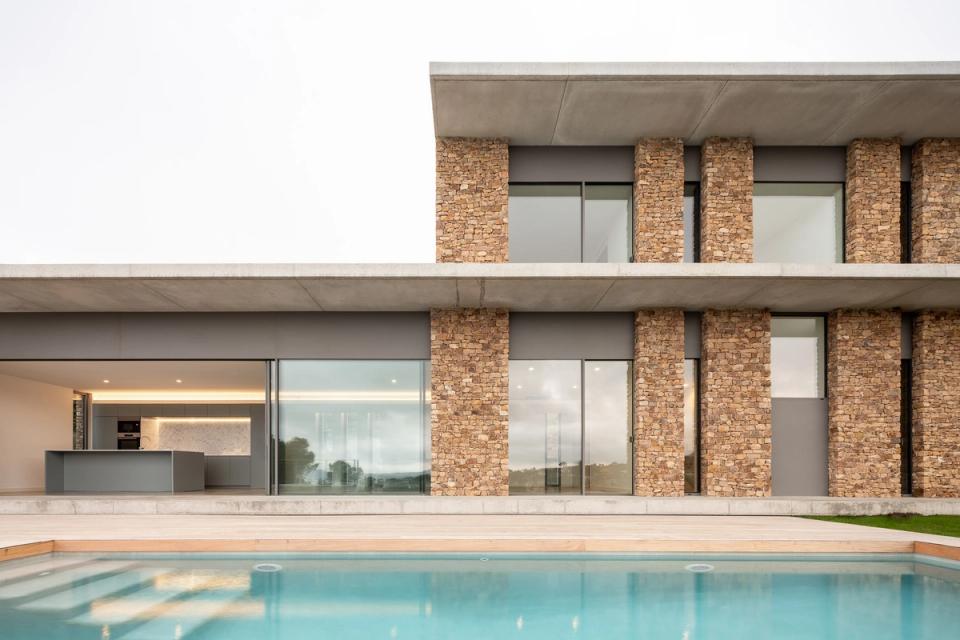Detached single-family home with straight lines and contemporary volumetry integrated into a sloping natural environment. The combination of white façades, natural stone, and wood creates an elegant and balanced image, strengthening the relationship between architecture and landscape.