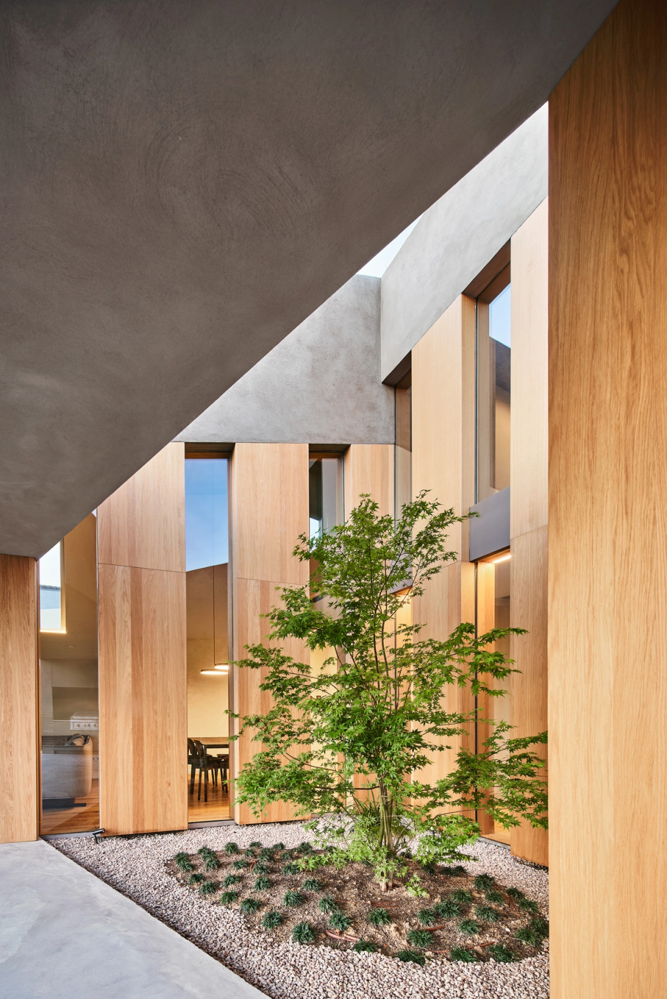 This single-family home incorporates an interior courtyard that acts as a transitional space between architecture and nature. Natural wood cladding, large vertical openings, and central vegetation provide warmth, light, and a tranquil atmosphere throughout the architectural ensemble.