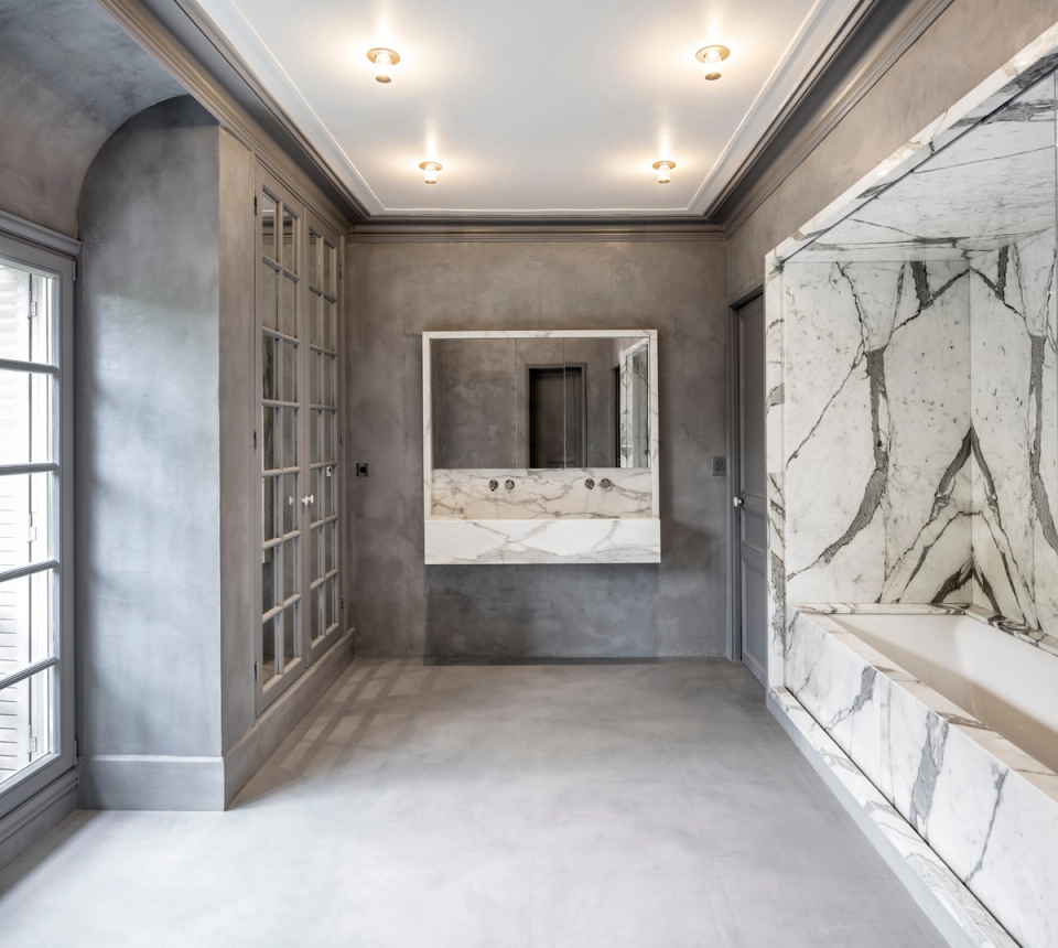 Interior renovation of a contemporary-style bathroom combining continuous gray surfaces with the elegant prominence of natural marble. The intervention enhances spaciousness and brightness through minimalist lines, integrated furniture, and a carefully selected palette of premium materials that provide sophistication and visual balance.