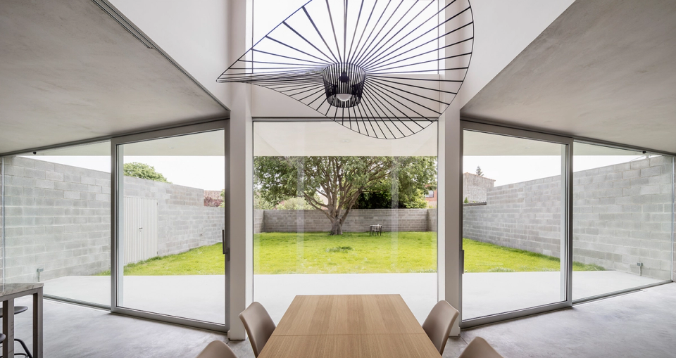 Dining space of a detached single-family home with double-height ceilings, large glass enclosures, and contemporary interior design. Natural light, open views of the garden, and minimalist finishes reinforce the feeling of spaciousness and connection with the outdoors.