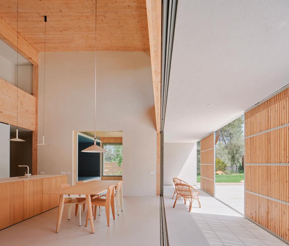 House in Girona with a fully open living area connecting interior and exterior through large sliding enclosures and wooden filters. This house in Girona combines natural light, warm materials, and spacious areas to create contemporary, comfortable architecture linked to the landscape