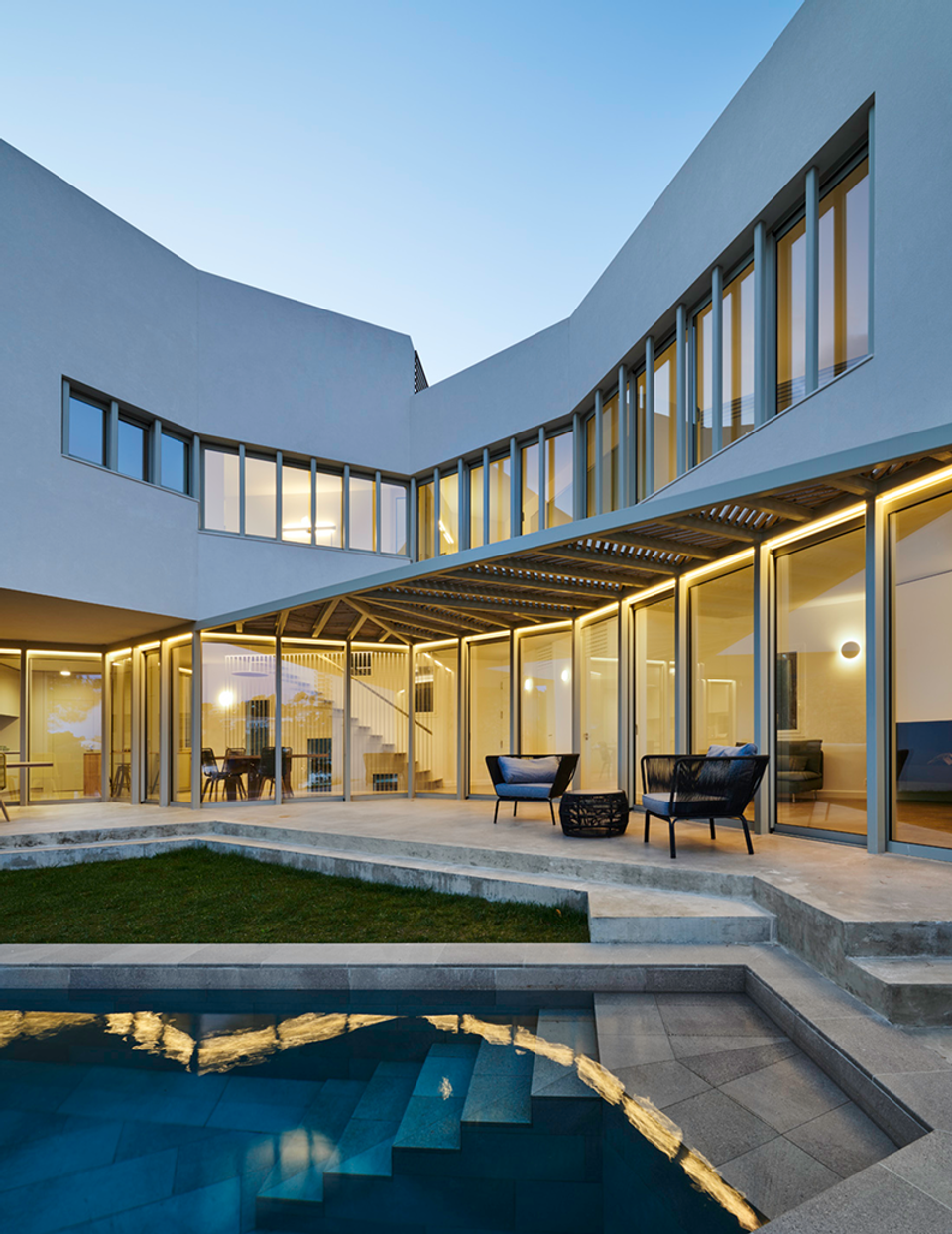Interior façade of a detached single-family home with swimming pool and large glass enclosures that enhance the relationship between indoor and outdoor spaces. The contemporary architecture stands out for its clean lines, integrated lighting, and a design focused on light, spaciousness, and residential comfort.