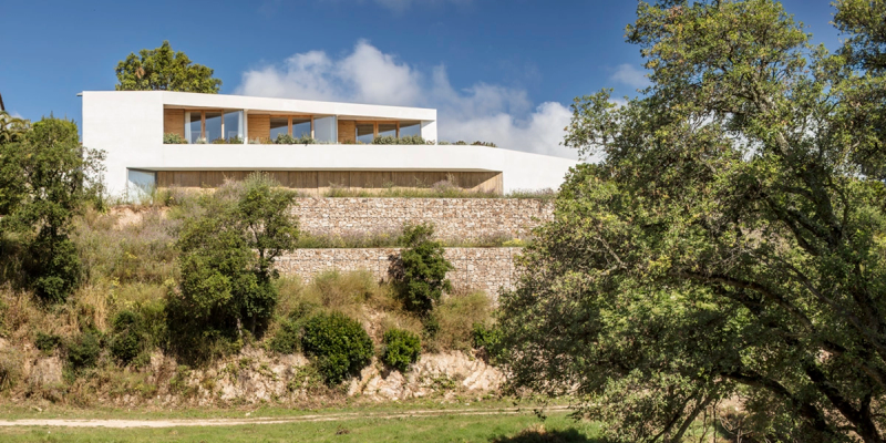  Luxurious Mediterranean style house, with white facade, integrated into the landscape. The wood colors of the huge windows are seen. Its green environments are characteristic of the area.