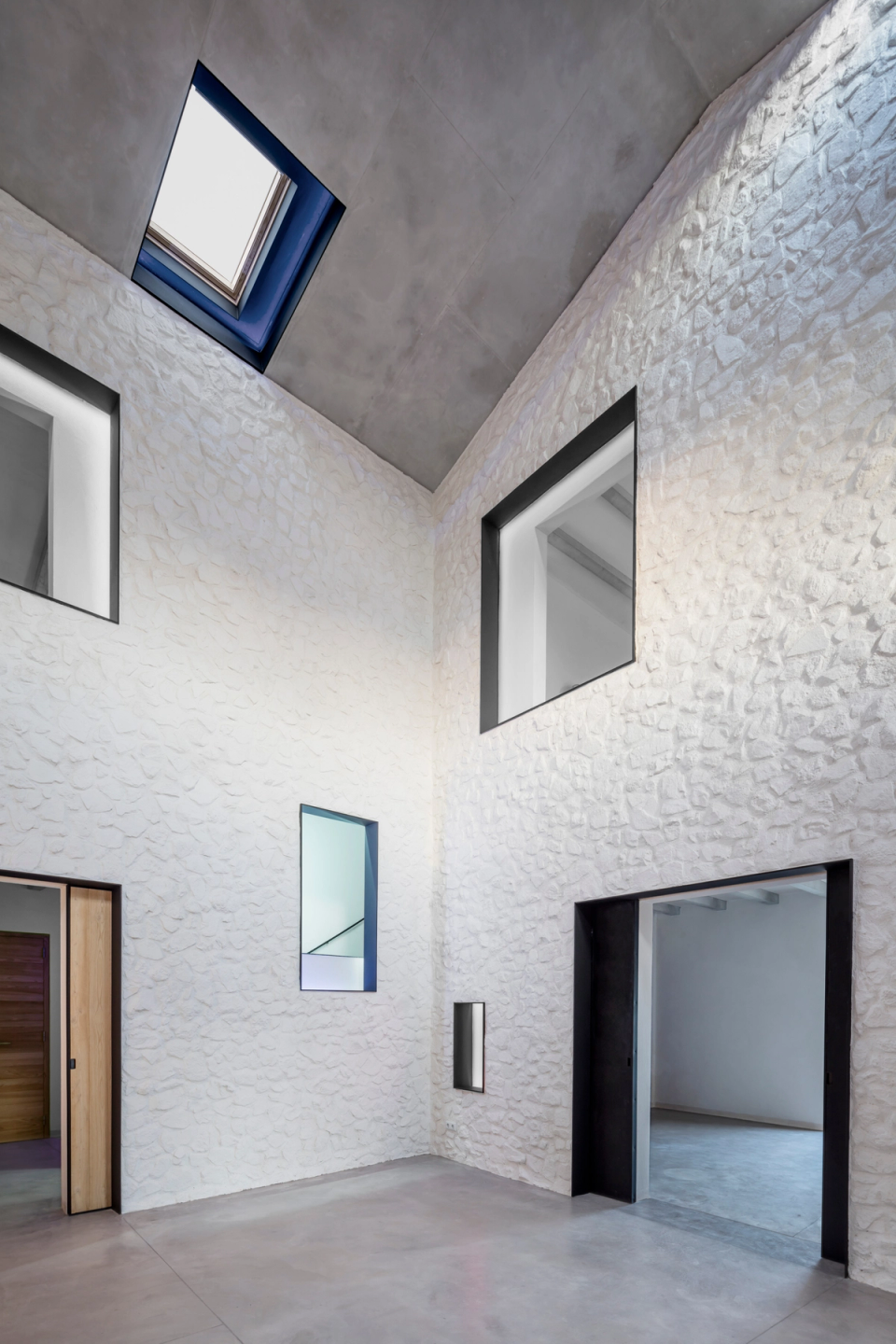 Interior courtyard of a comprehensive renovation with restored stone walls and contemporary architecture that prioritizes natural light and visual spaciousness. Integrated skylights in the sloped ceilings allow zenithal light to highlight the textures of the stone and add depth to the spaces. Geometric openings visually connect the different rooms, creating a fluid, elegant, and functional layout. This full renovation combines tradition and modernity through noble materials, minimalist finishes, and a timeless aesthetic focused on comfort and brightness.