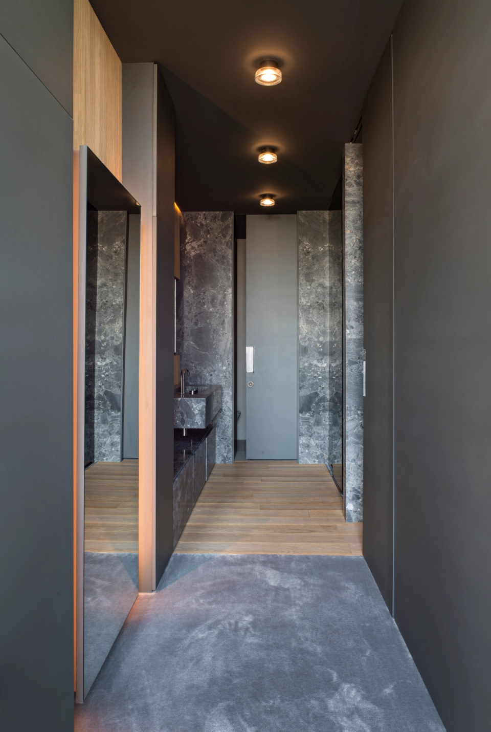 The interior renovation of this transitional and bathroom area embraces a contemporary and sophisticated aesthetic, defined by the use of dark materials, natural stone, and integrated lighting that enhances the depth of the space. Continuous surfaces and minimalist lines create a sense of order and elegance, while contrasts between warm textures and mineral finishes add character and exclusivity. The design carefully considers every detail to transform circulation spaces into a coherent, functional, and visually striking architectural experience.