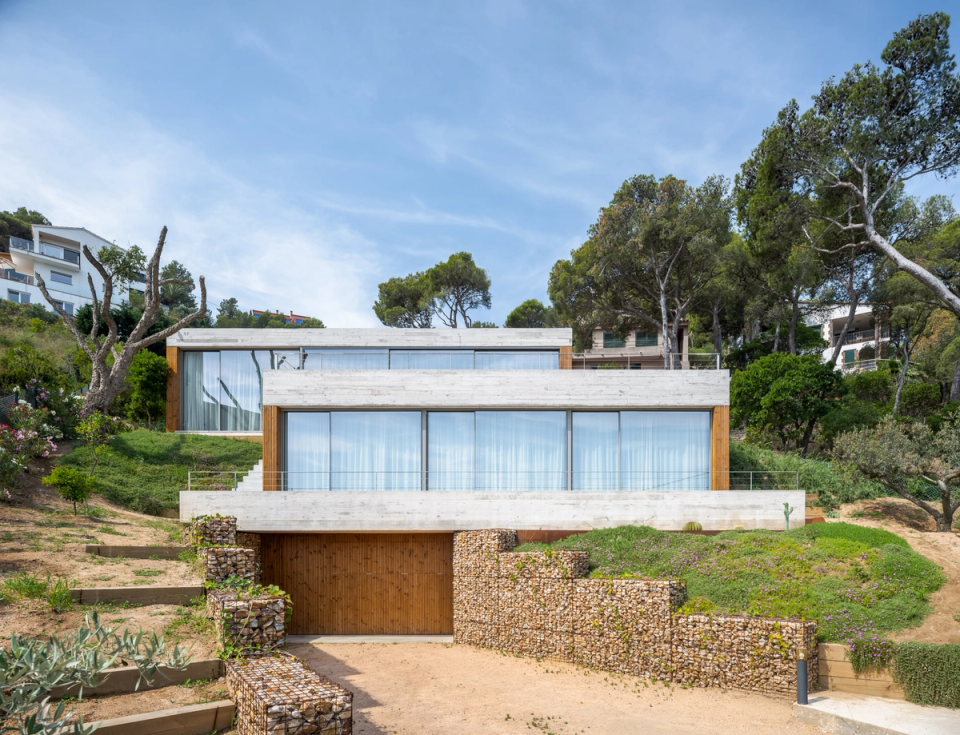 This single-family home in Begur stands out for its contemporary architecture integrated into the Mediterranean landscape, featuring horizontal lines, large openings, and natural materials that reinforce the connection with the surroundings. The project adapts elegantly and functionally to the sloping terrain, taking advantage of the views and natural light to create spacious, open spaces fully connected to the outdoors.