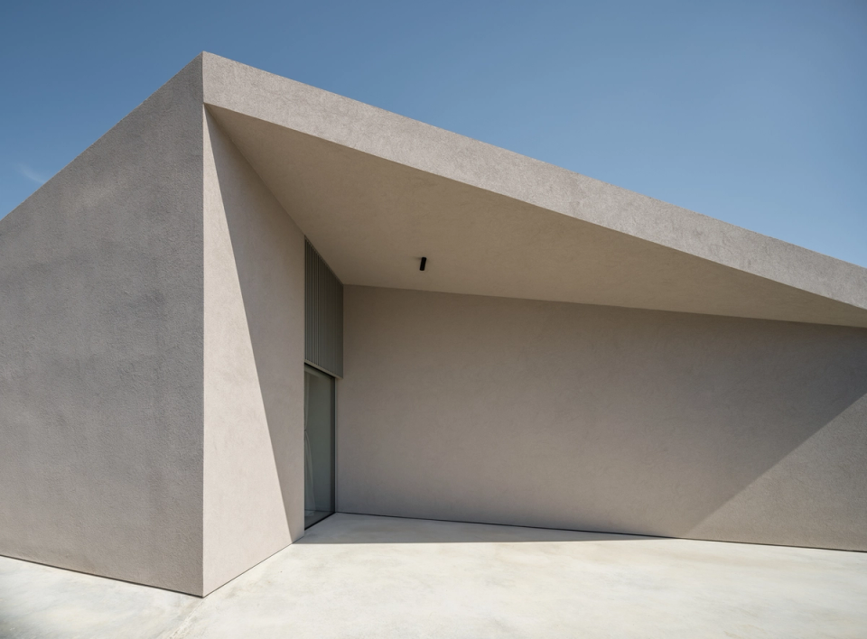 This single-family home stands out for its architectural expressiveness based on pure geometries, inclined planes, and a sculptural volumetry with strong visual impact. The use of continuous materials and neutral tones reinforces a sense of sobriety and elegance, creating a minimalist project that plays with light, shadows, and the depth of outdoor spaces.