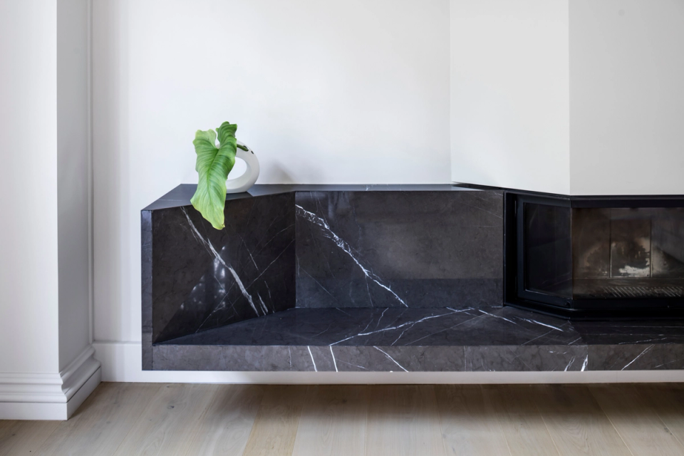 Interior renovation detail focused on a contemporary fireplace clad in dark natural stone, bringing elegance and prominence to the space. The intervention combines minimalist lines, premium materials, and precise finishes to create a sophisticated, warm atmosphere perfectly integrated with the interior architecture of the residence.