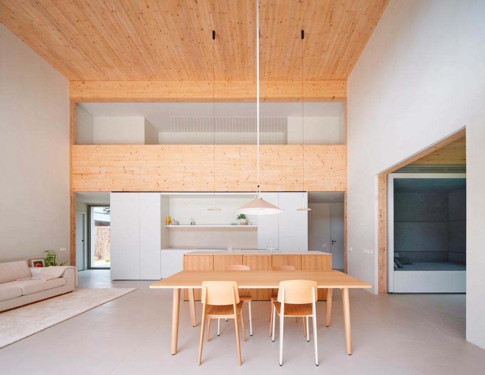 House in Girona with a large double-height central space organizing the kitchen, dining room, and living areas into a single open environment. This house in Girona combines minimalist architecture, natural wood, and zenithal light to create a warm, functional, and contemporary atmosphere