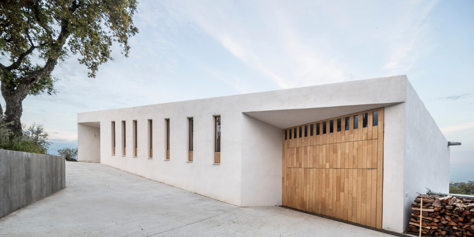 Exterior detail of a detached house with architecture integrated into the landscape, where white volumes and natural cladding create a serene and contemporary image. Mediterranean vegetation, organic textures and pure lines reinforce the connection between the home and its natural surroundings.